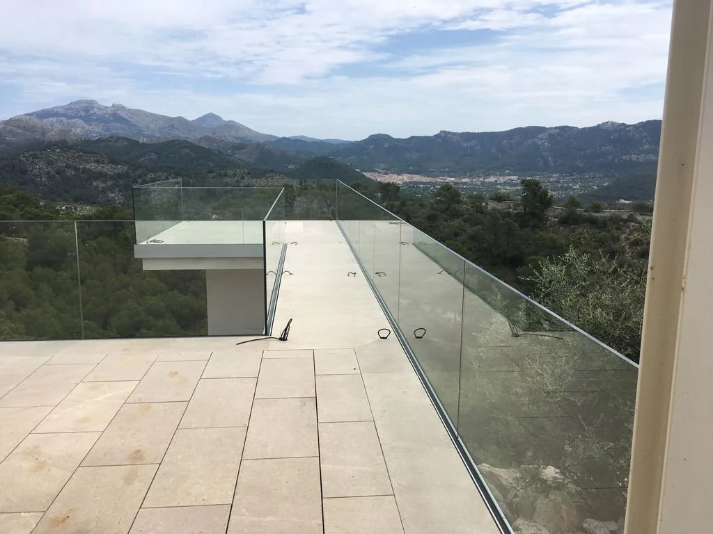 Balcón con barandal de cristal con vista a montañas y vegetación en un día nublado.