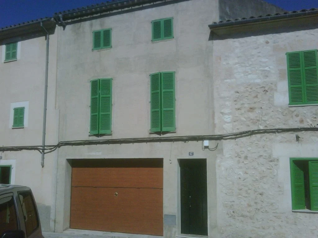 Edificio de varias plantas con paredes de piedra y ventanas con persianas verdes.