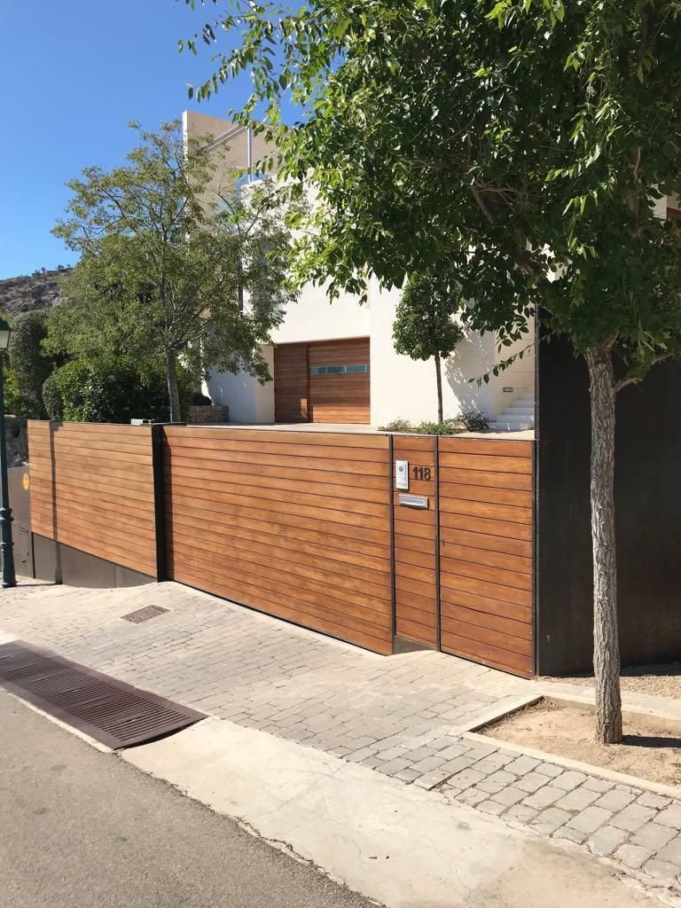 Casa moderna con muro de madera y portón de madera en la entrada, rodeada de árboles y en un barrio residencial.