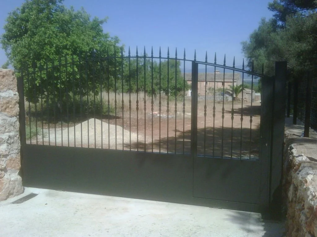 Puerta de reja metálica negra en un portal con paredes de ladrillo.