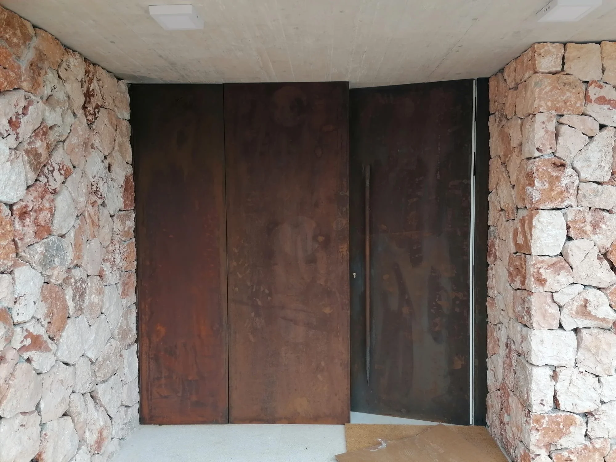 Puerta de metal oscura entre paredes de piedra y muro de cemento en un interior moderno.