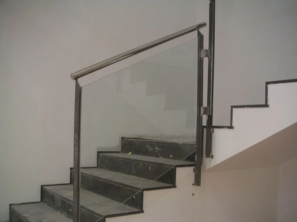 Escalera interior en construcción con barandal de metal y paredes blancas.