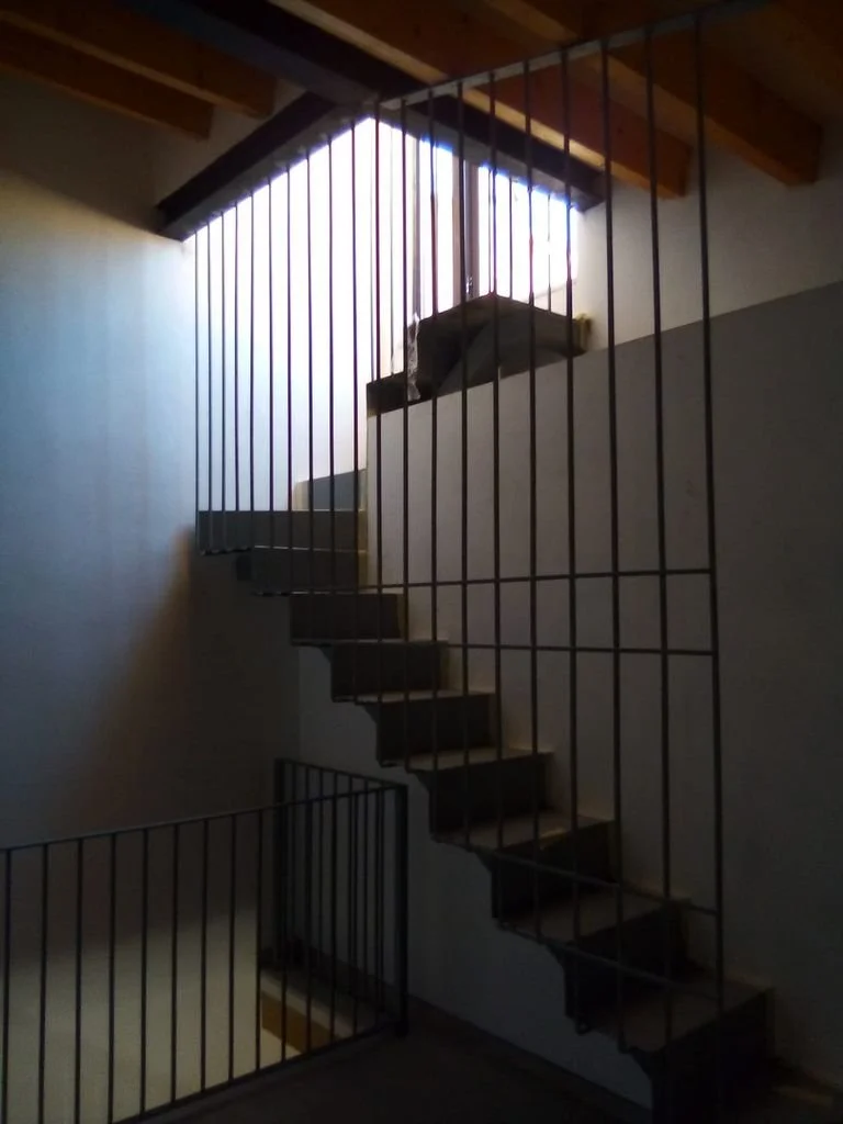 Escalera de caracol de madera con barandilla de metal en interior con ventanas que dejan entrar luz.