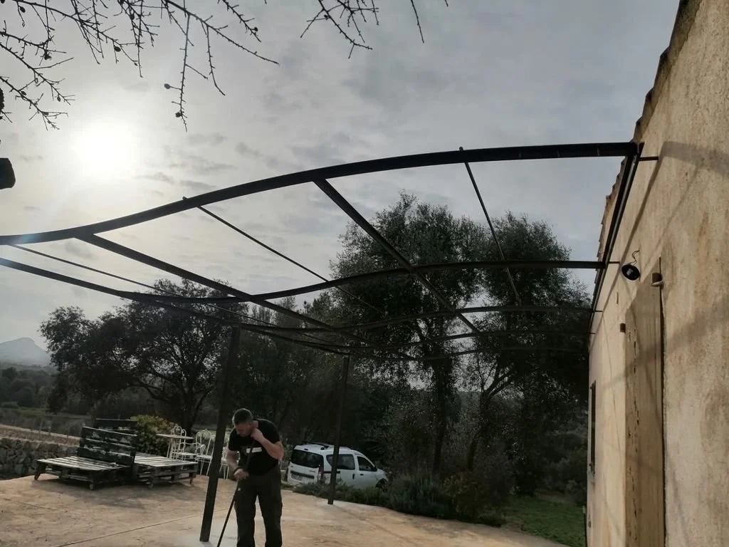 Hombre limpiando en un patio al aire libre con árboles y un vehículo en el fondo, bajo un cielo nublado.