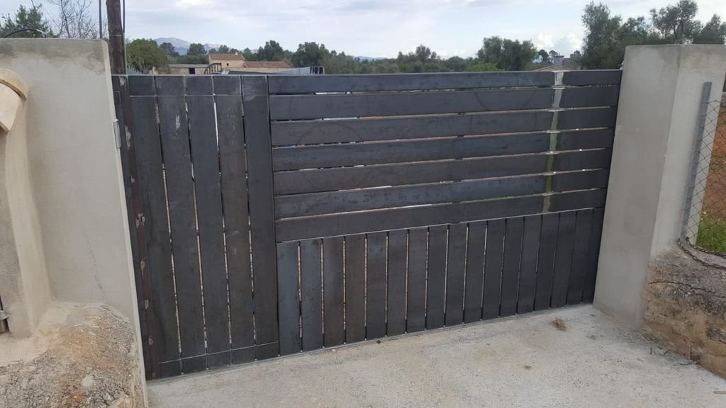Puerta de madera negra en una entrada cerrada, con pilares de cemento a los lados.