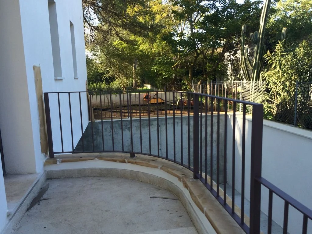 Barandal negro en construcción en un balcón con vista a árboles y vegetación en un espacio exterior.