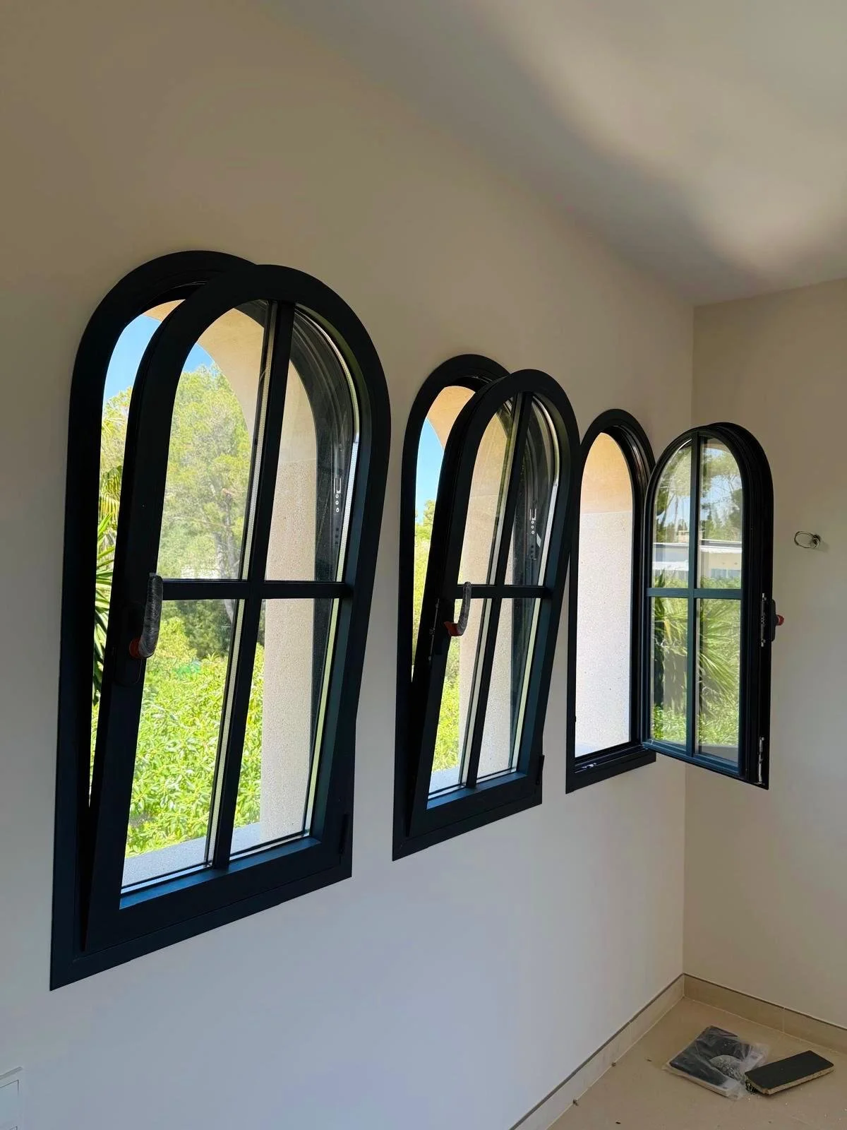 Cuatro ventanas arqueadas en una pared de interiores con vista a árboles verdes.