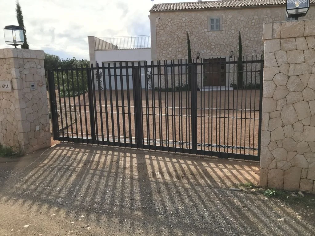 Puerta de reja negra en entrada de casa con muro de piedra