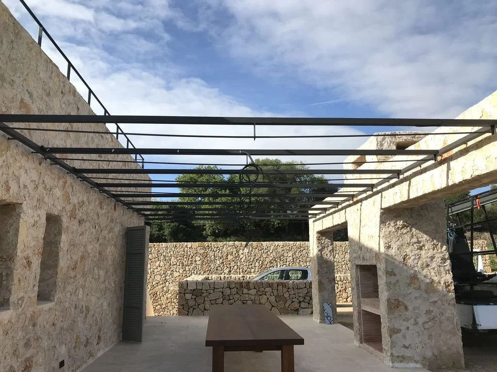 El interior de una estructura en construcción con paredes de piedra y un techo sin techo, con un coche estacionado en el fondo y un cielo parcialmente nublado.