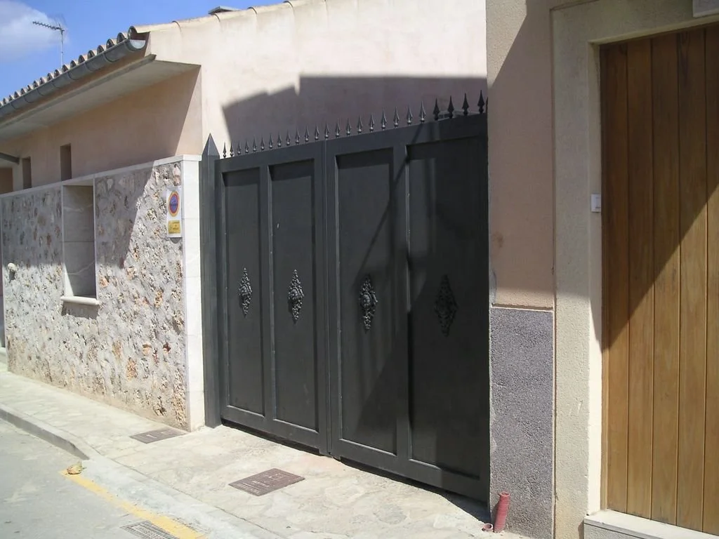 Puerta y muro de entrada a una casa con pared de piedra y puerta negra con picos decorativos