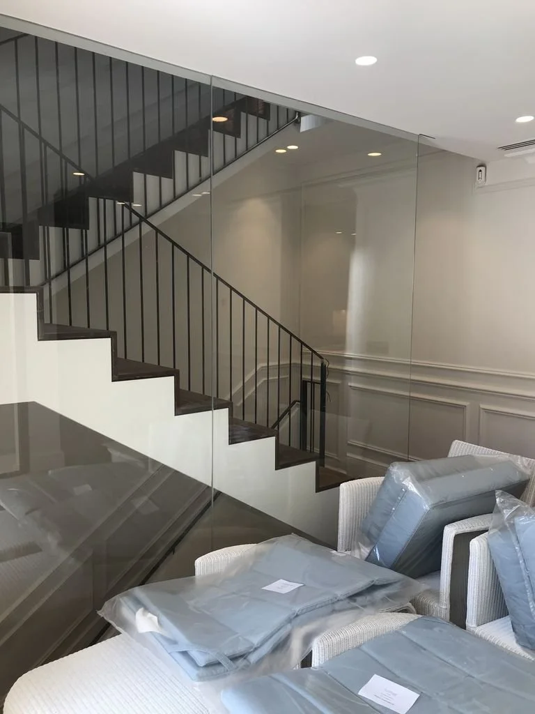 Sala de estar con sillas, algunos productos envueltos en plástico, y una escalera metálica con barandilla negra en un espacio moderno