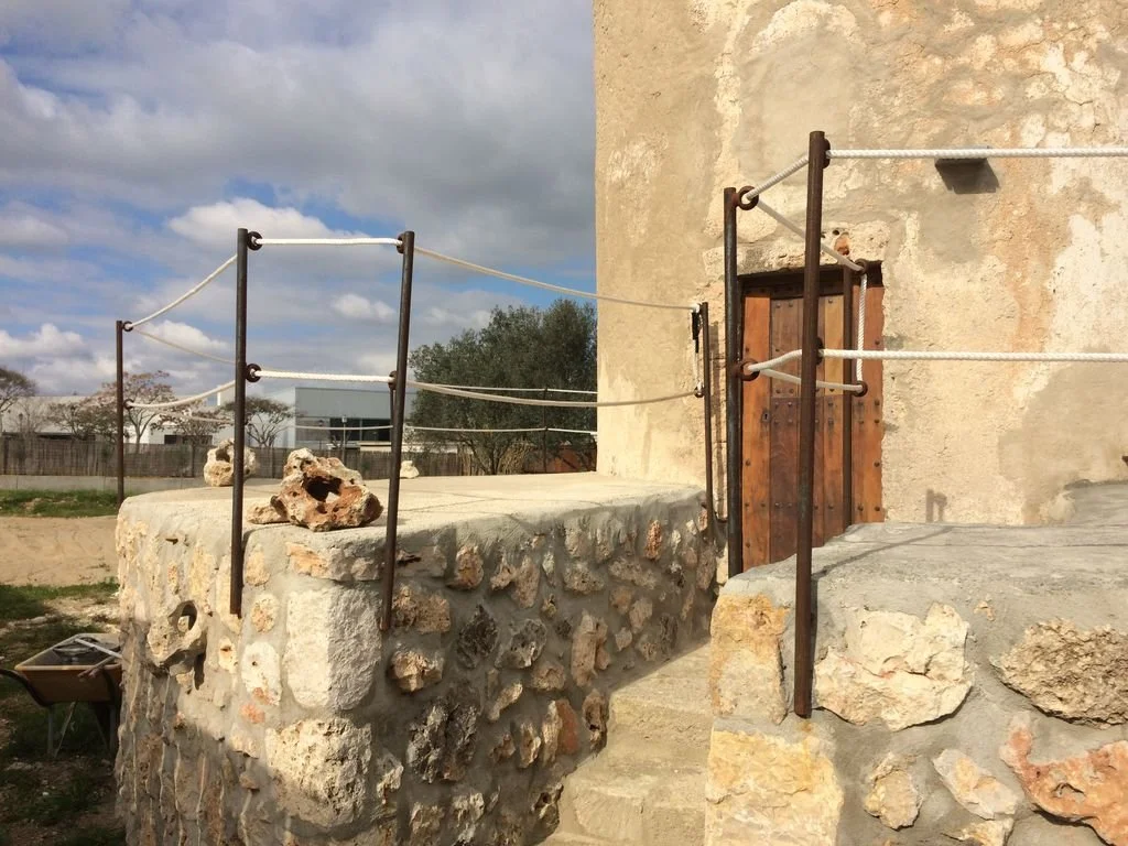 Estructura de escalera con barandas de cuerdas en un edificio de piedra de aspecto rústico, frente a un cielo nublado.