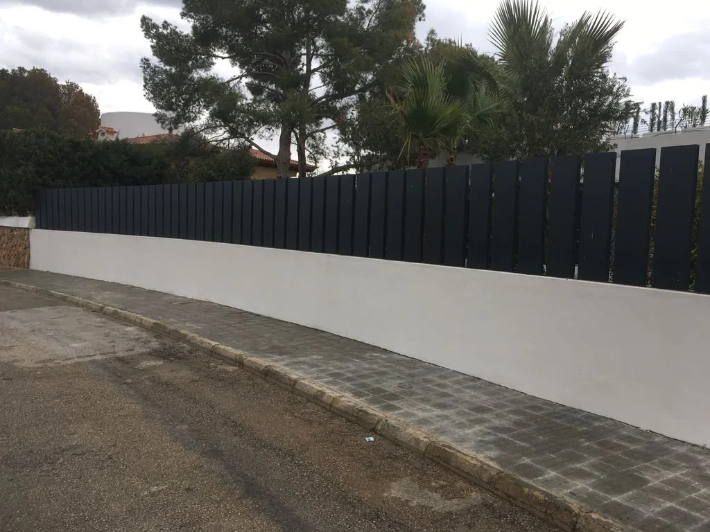 Muro de reja negro y muro de concreto blanco en una calle con acera de piedra.