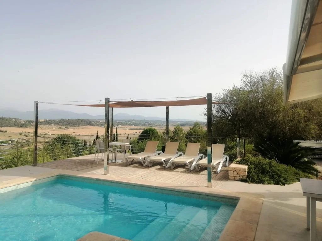 Piscina en una terraza con vista panorámica a los campos y montañas, sombrilla de sombra, sillas reclinables y mesas.