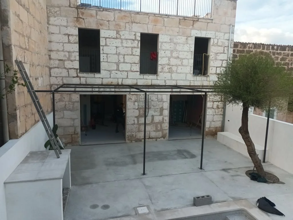 Patio en construcción con estructura metálica y un árbol en el lado derecho.
