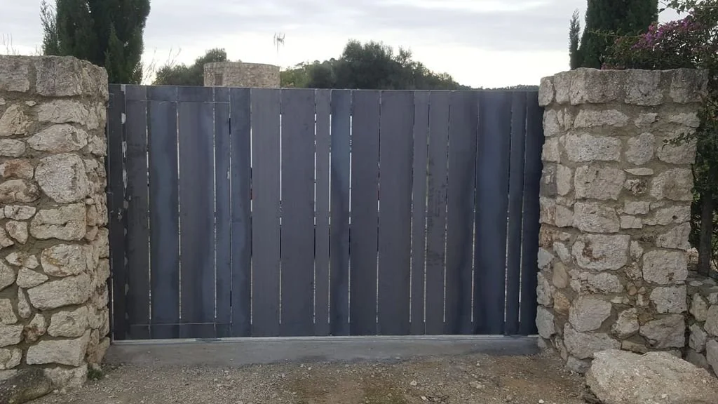 Puerta de madera gris enmarcada por muros de piedra.