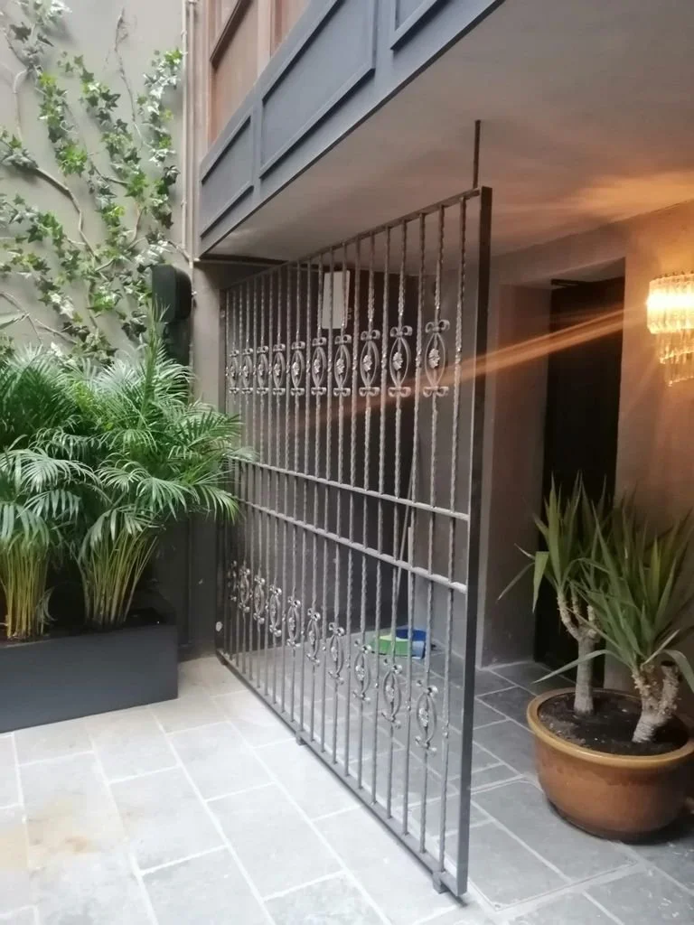 Puerta de rejas de metal decorativa en un patio con plantas en macetas.