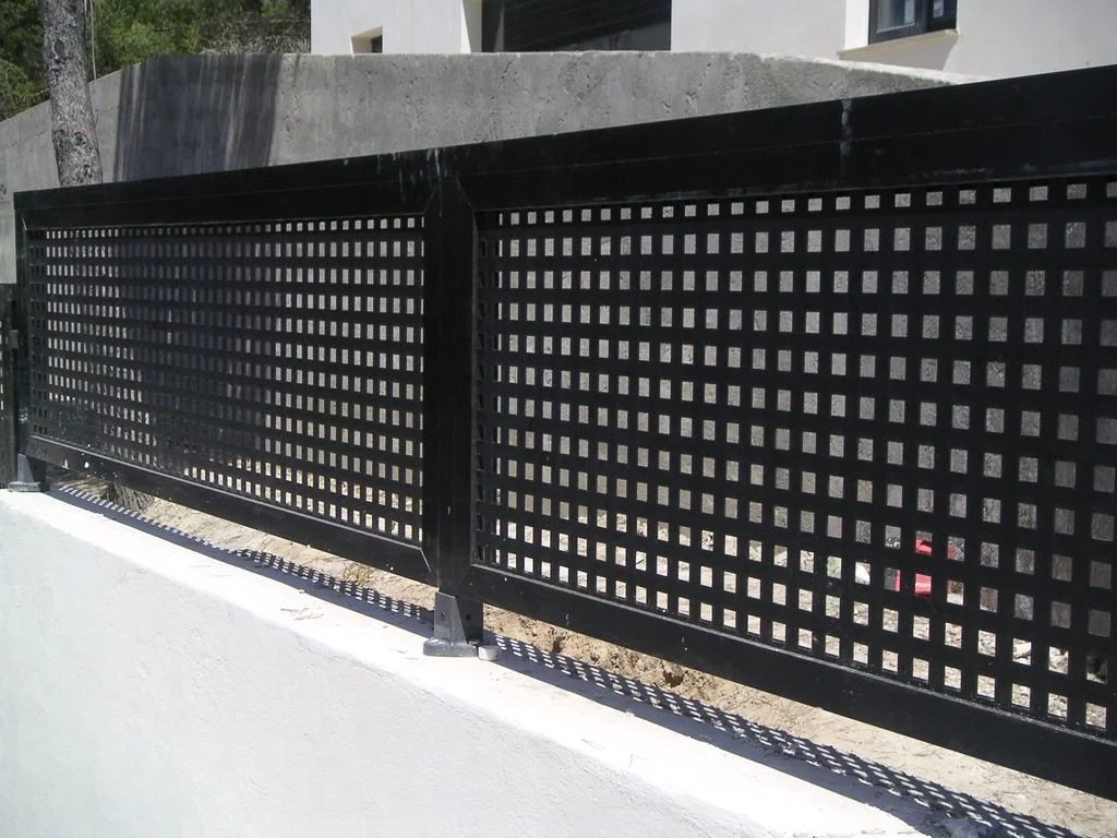 Valla de metal negra con patrón de cuadros, situada en la orilla de una acera en un área urbana.