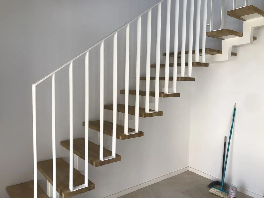Escalera moderna de madera y barandilla blanca en interior de casa.