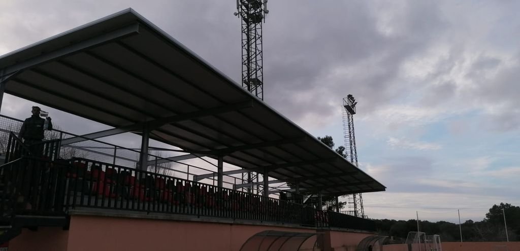 Estructura de un estadio con gradas, barandales y torres de iluminación bajo un cielo nublado.