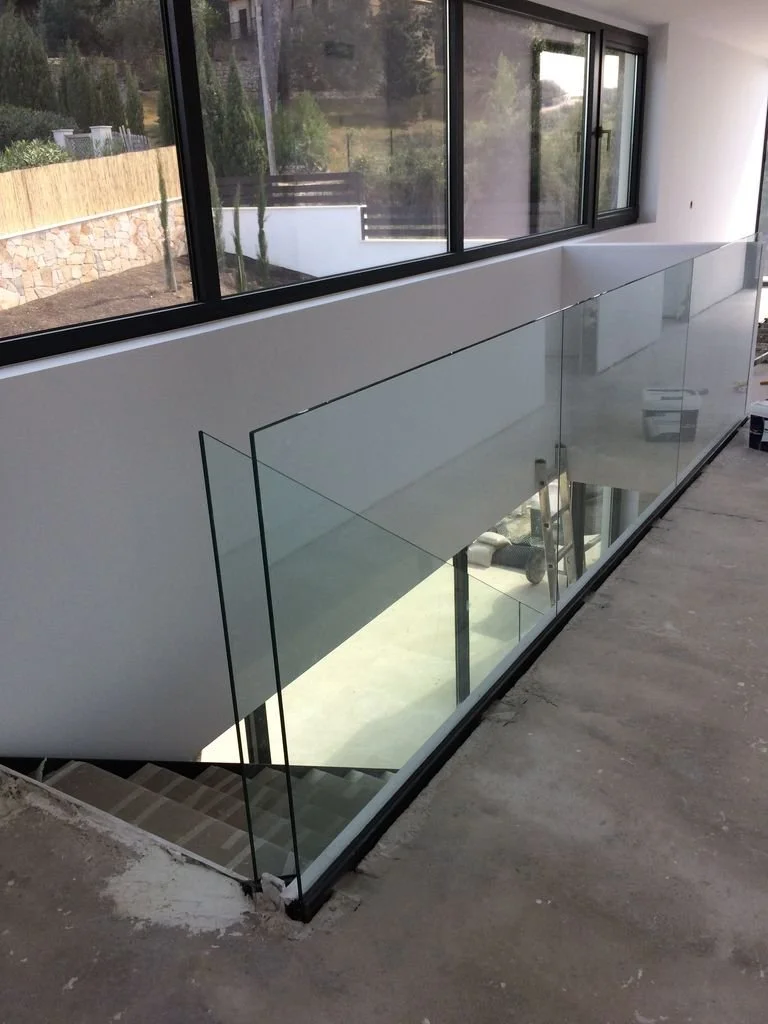 Escalera y una barandilla de vidrio en una casa en construcción con ventanas grandes y vista exterior.