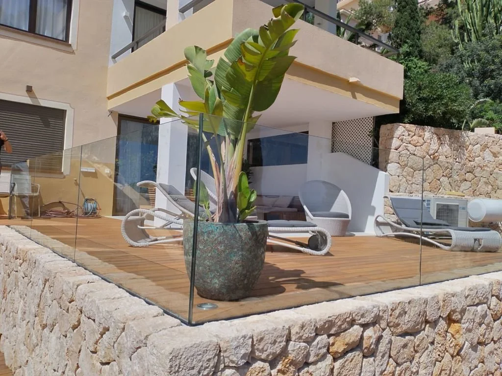 Terraza en un edificio moderno con plantas, sillas de mimbre, una decoración simple y vistas a áreas verdes exteriores.