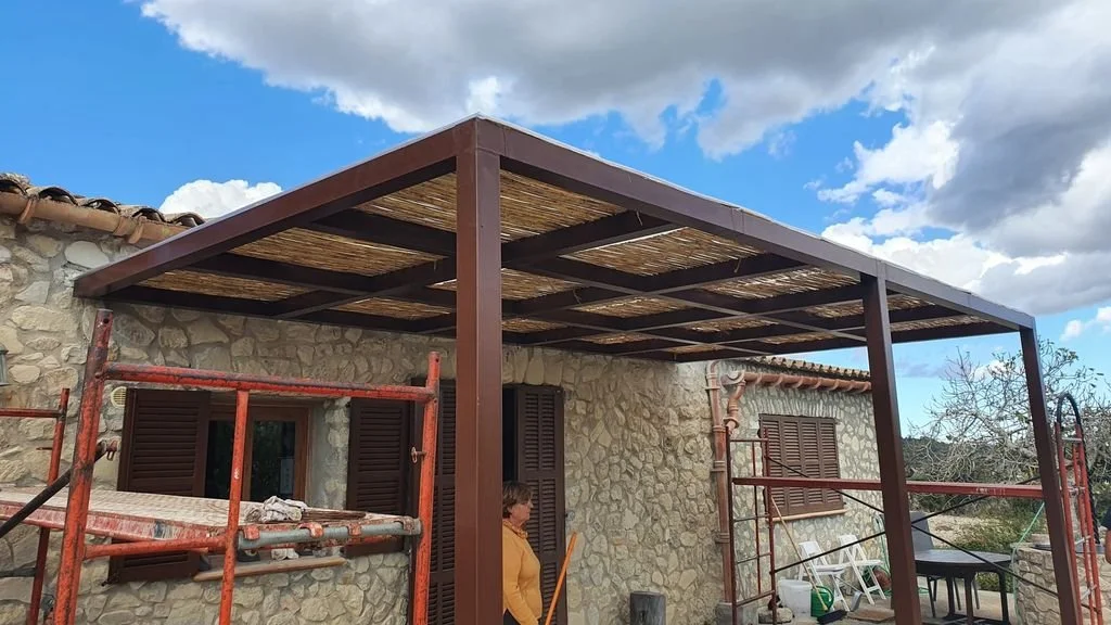 Casa de piedra en construcción con estructura de madera para un porche o cubierta, andamios y herramientas en el sitio.