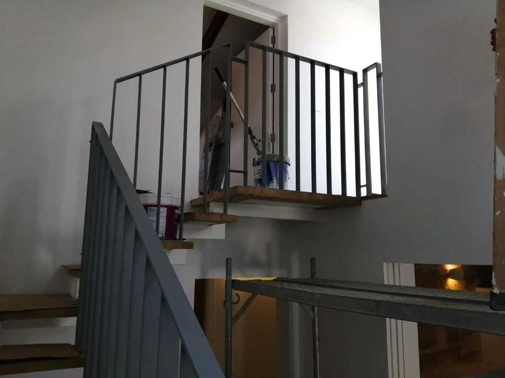 Escalera en construcción con barandales de metal y accesorios de pintura en un interior de casa en remodelación.