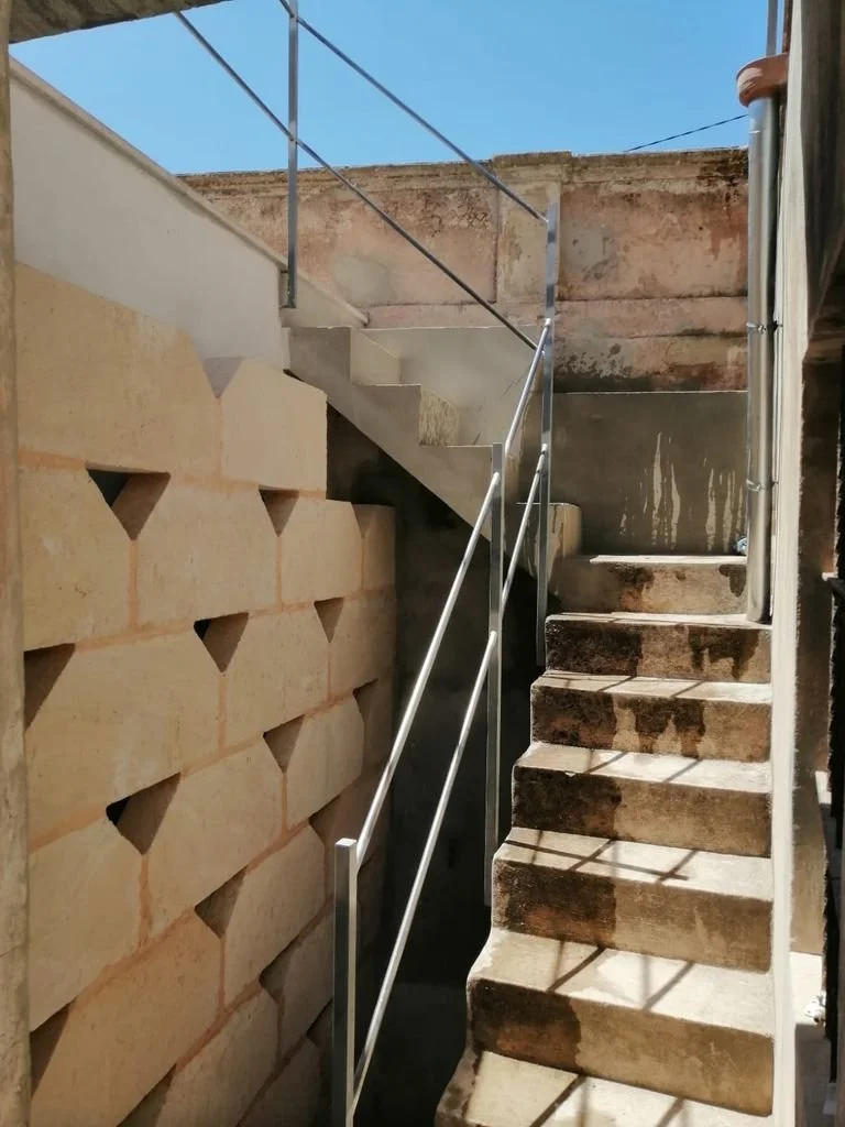 Escalera de concreto en un área de construcción o reforma, con una pared de bloques decorativos y cielo visible en el fondo.