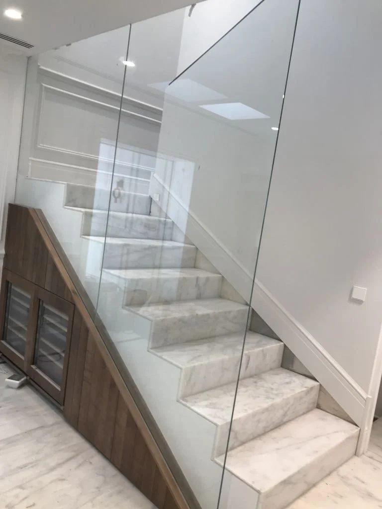 Escalera de mármol con barandal de vidrio en interior moderno.