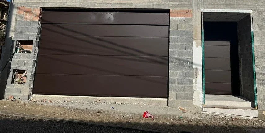Puerta de garaje de seguridad y entrada principal en construcción, en una fachada de ladrillos y bloques de cemento.