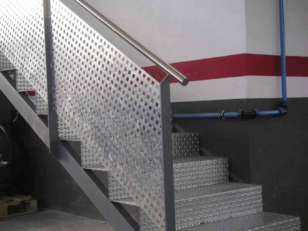 Escalera de metal con pasamanos en un estacionamiento o área de servicio, con paredes pintadas en blanco, rojo y negro