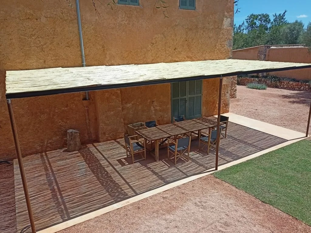 Mesa de comedor de madera con siete sillas en una terraza con sombra."