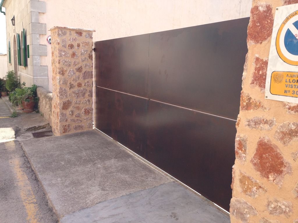 Gran puerta negra de metal en una entrada con paredes de piedra y una señal de tránsito en una pared de ladrillos.