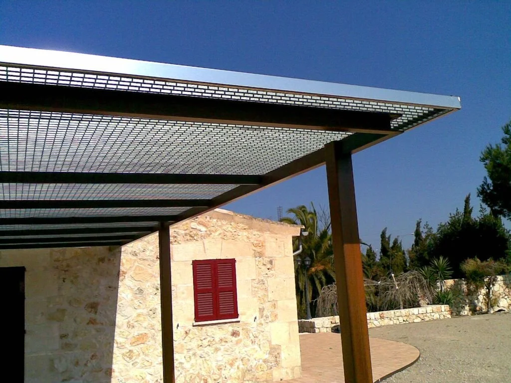 Estructura de metal cubriendo un área al aire libre, en un entorno de casa con paredes de piedra y plantas