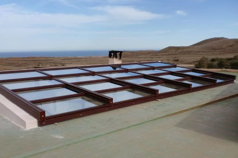 Ventanas de acrílico o vidrio en el techo de un edificio, con un paisaje de campo y mar de fondo.