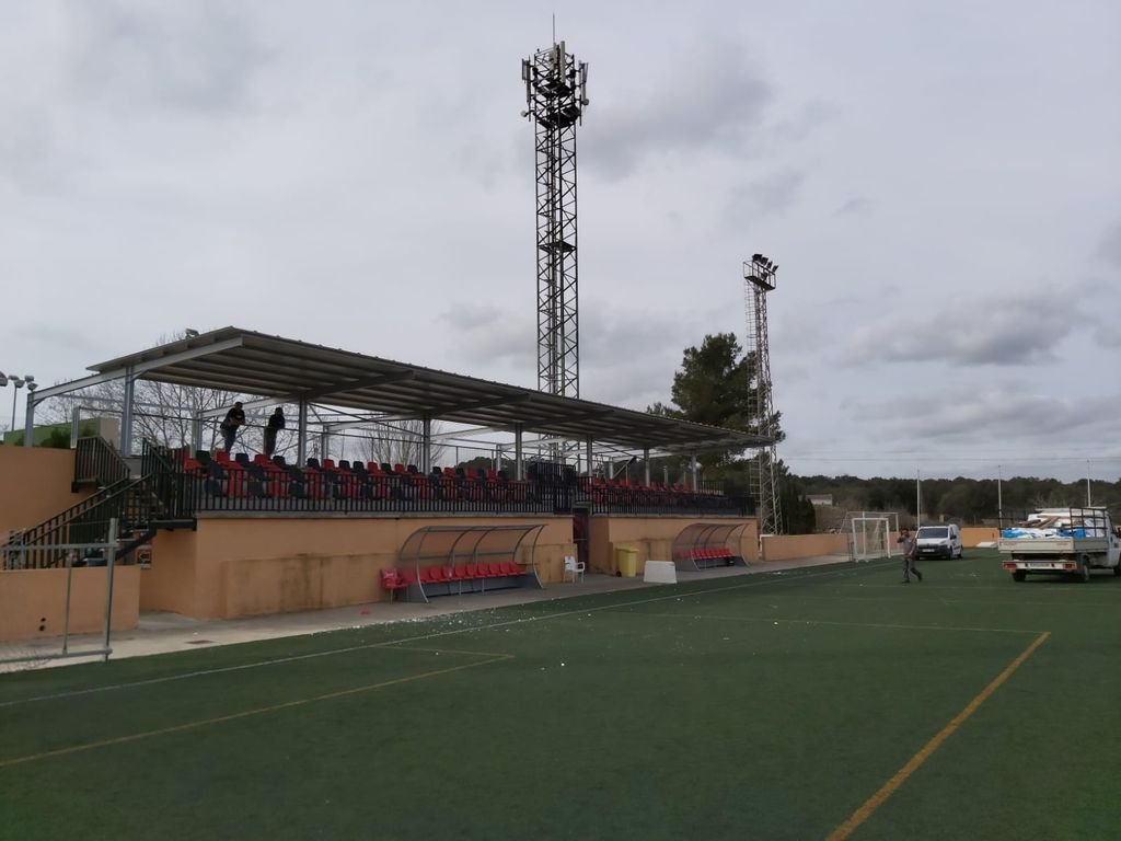 Estadio de fútbol con gradas cubiertas, teléfonos de transmisión, campo y personas.