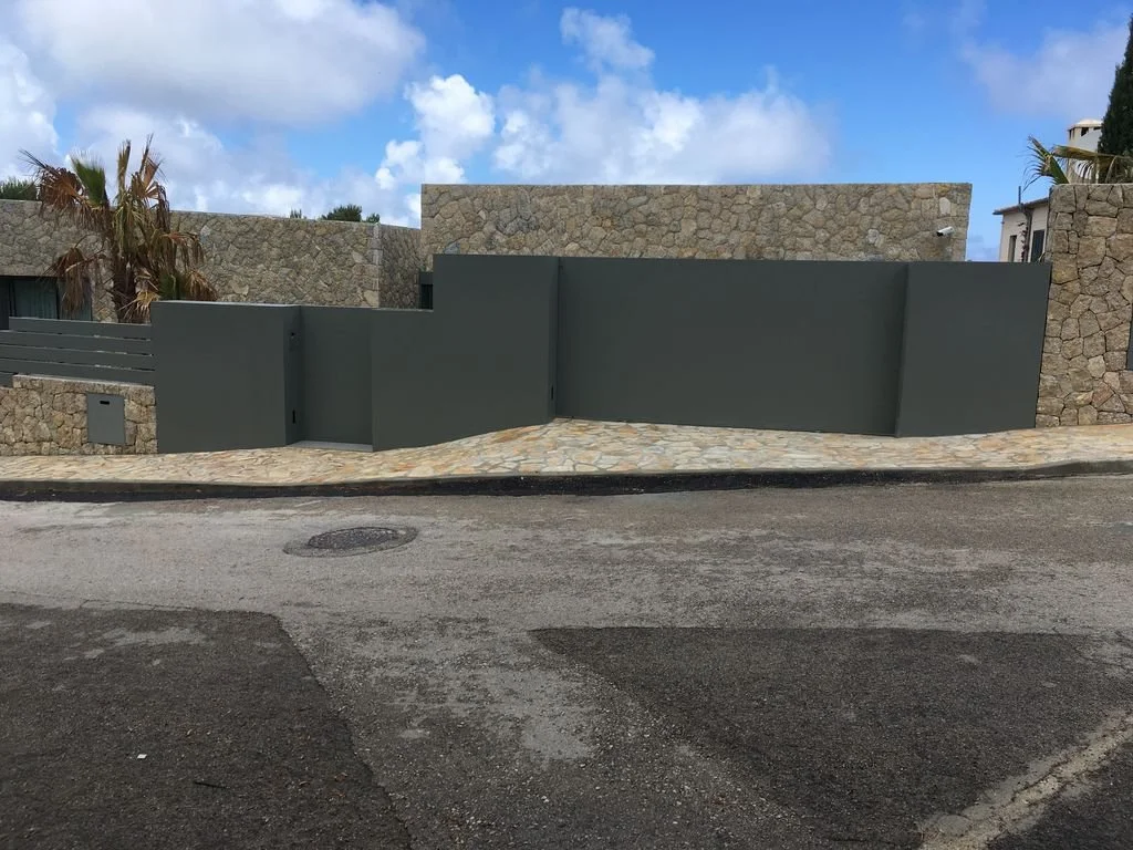Muro de paredes de piedra y muro de color gris en el frente de una casa moderna, con acera de piedra y calle de pavimento oscuro.