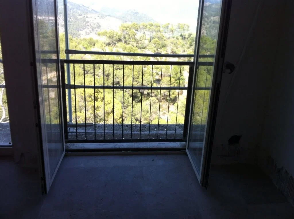 Vista de un balcón con barandilla metálica, con vista a un paisaje de árboles y montañas al fondo.