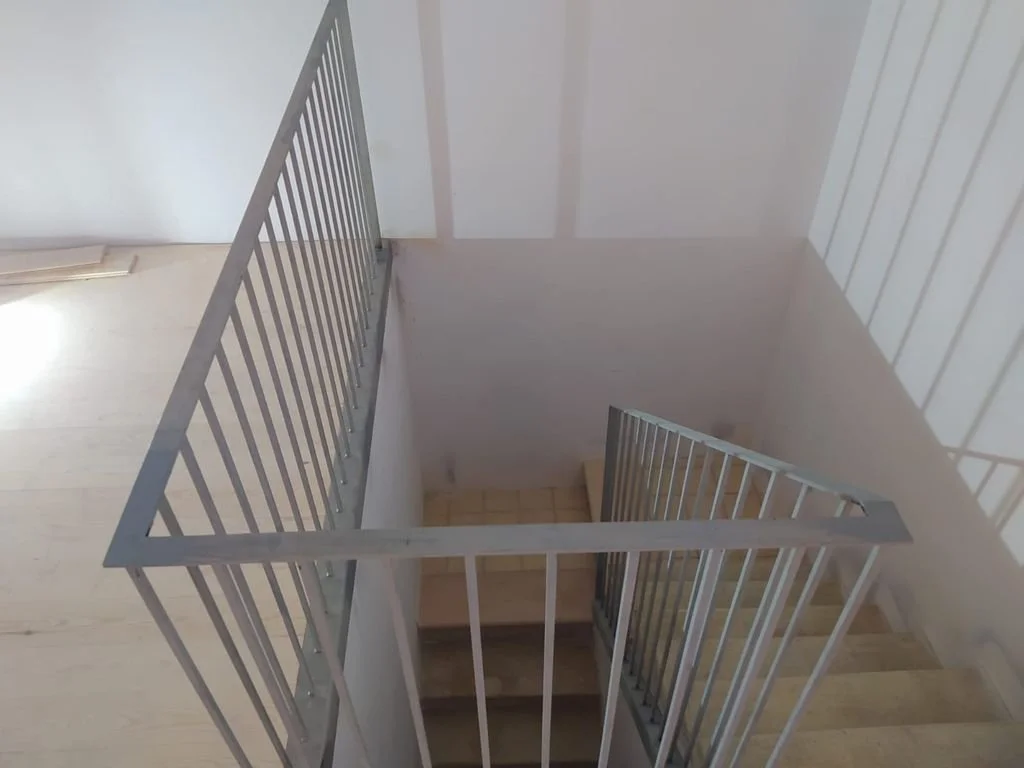 Vista de una escalera vista desde arriba, con barandillas de metal y pasos de madera.