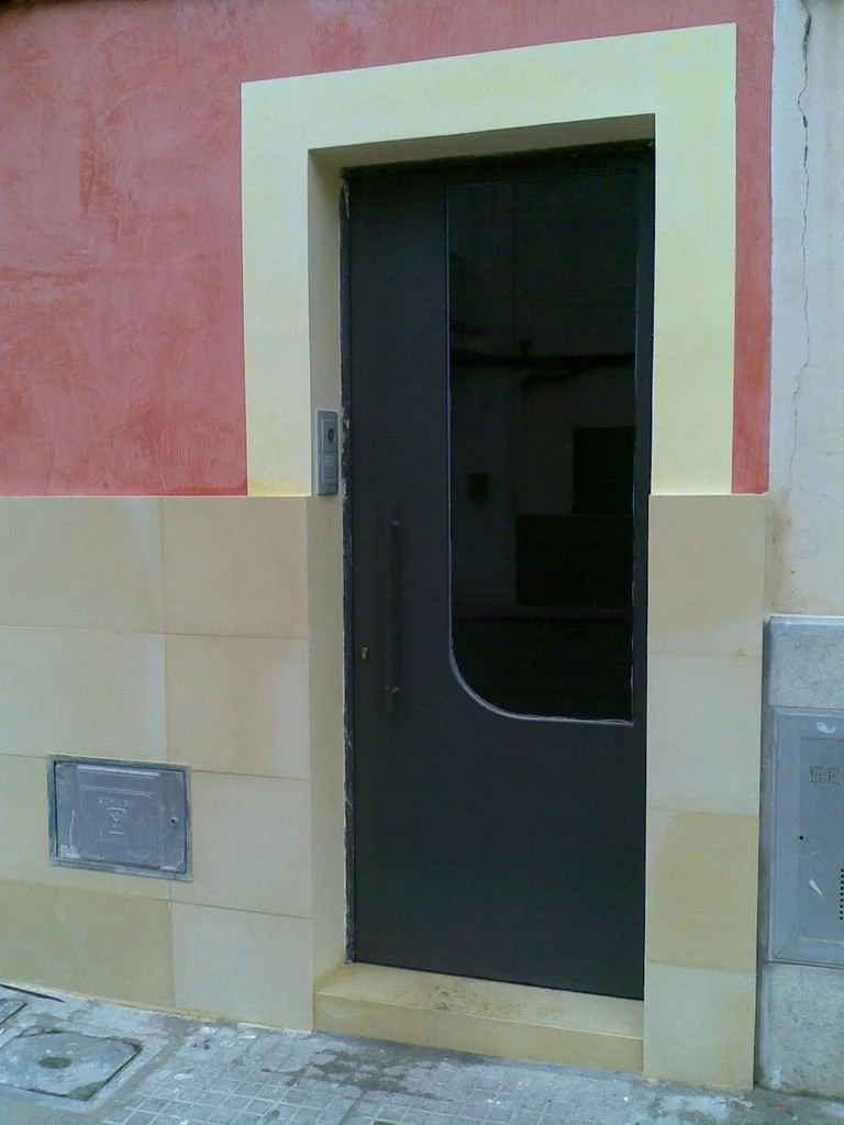 Puerta de ascensor en el interior de un edificio con paredes de colores y una pequeña plataforma de entrada.
