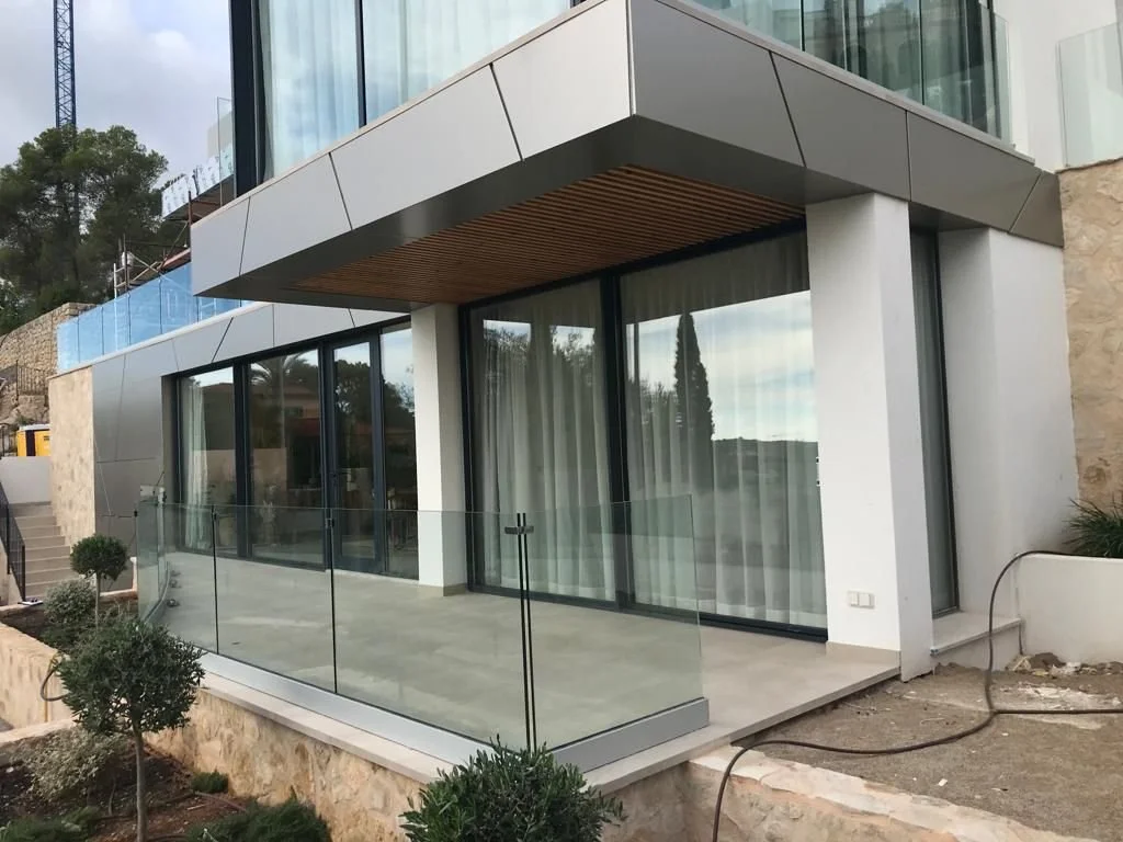 Fachada moderna de casa con balcón de cristal y ventanas grandes.
