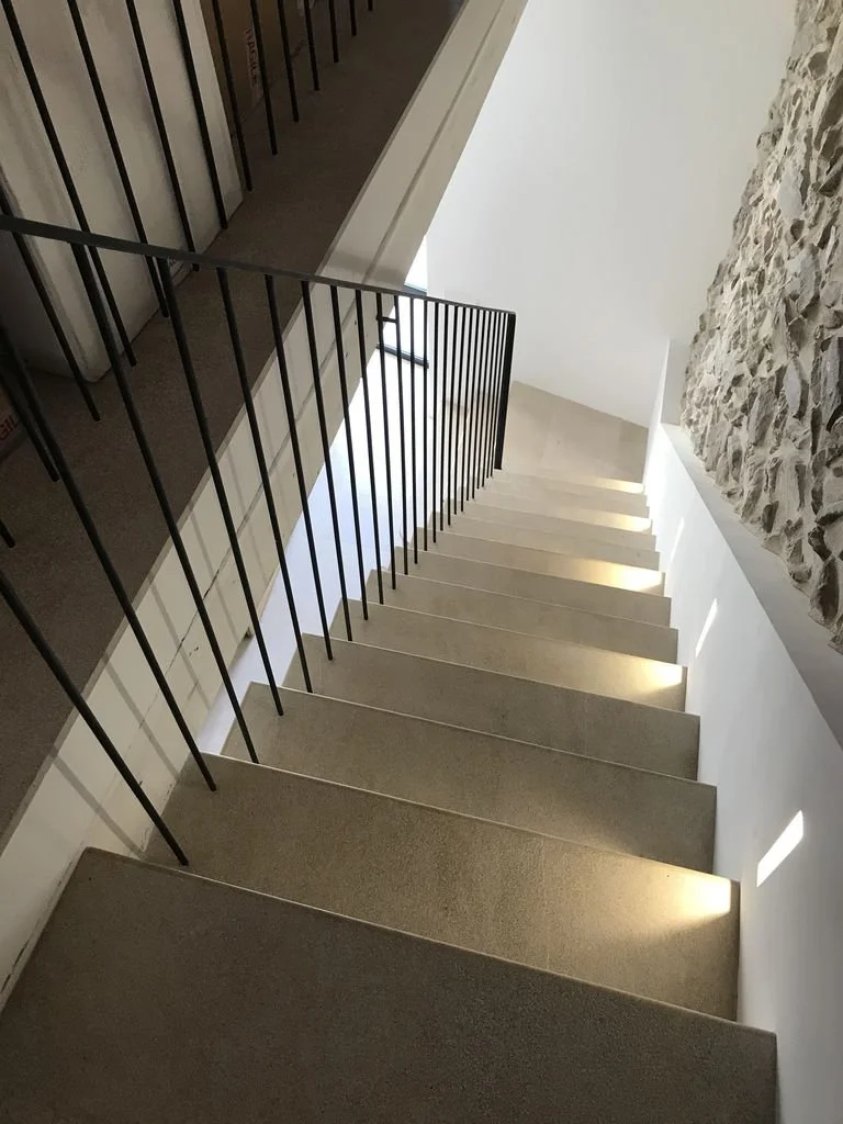 Escalera interior con barandilla negra y pared de piedra a un lado.