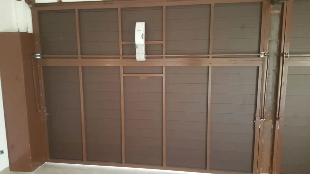 Estructura de la puerta de un garaje en construcción con revestimiento de madera y un sistema de apertura automatizado.