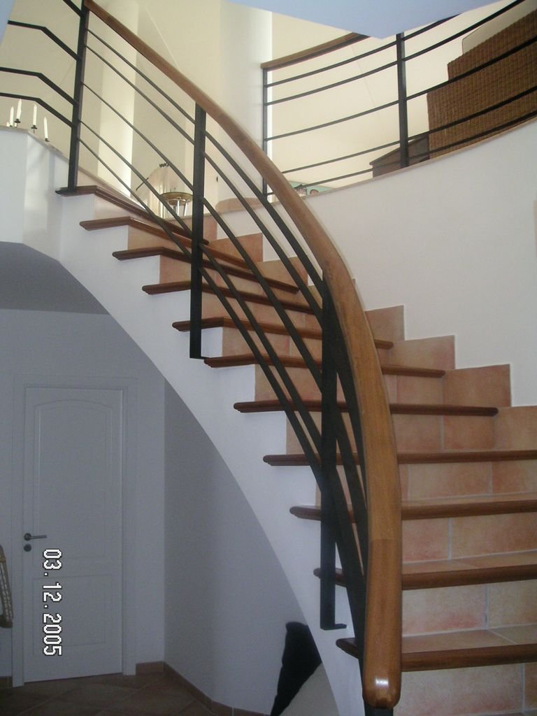 Escalera de caracol interior con barandilla de madera y barandillas negras de metal en una casa moderna.