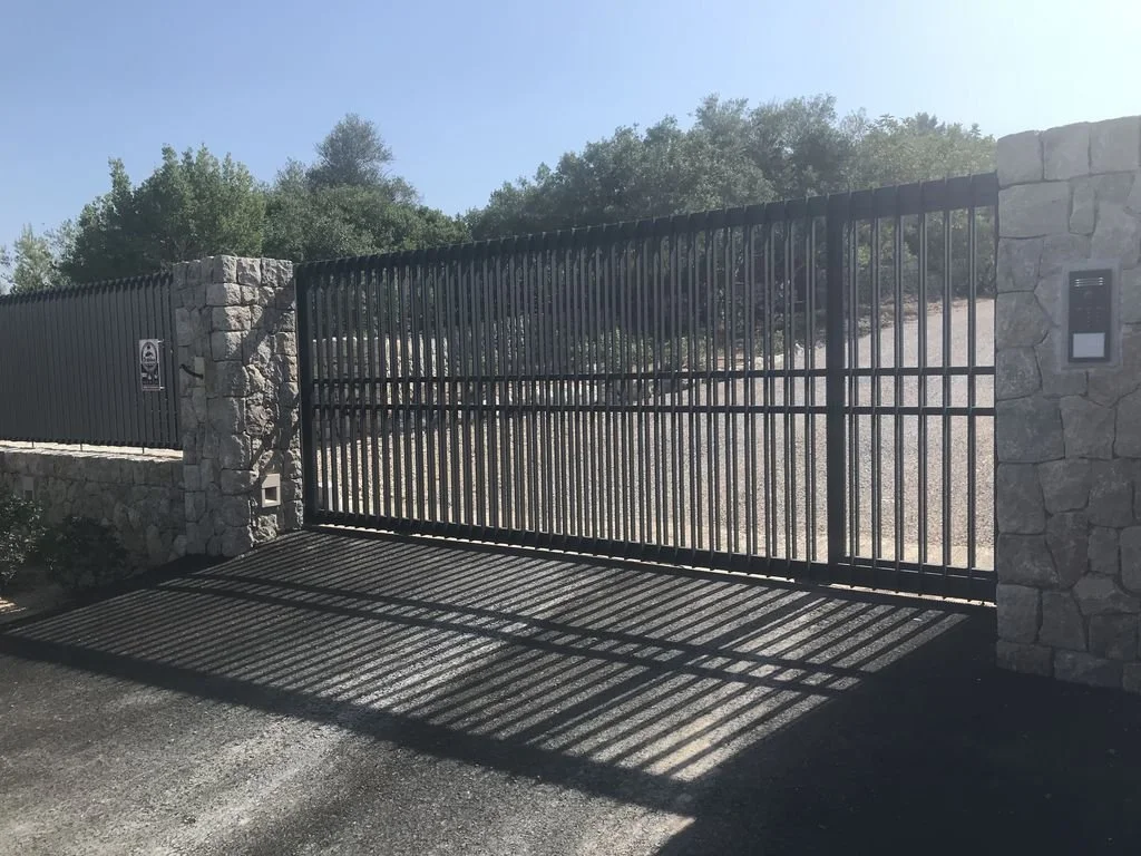 Reja de entrada de metal con sombra proyectada en el suelo y paredes de piedra