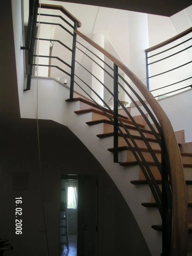Escalera en espiral de madera y metal en interior de casa con barandas negras y pared blanca