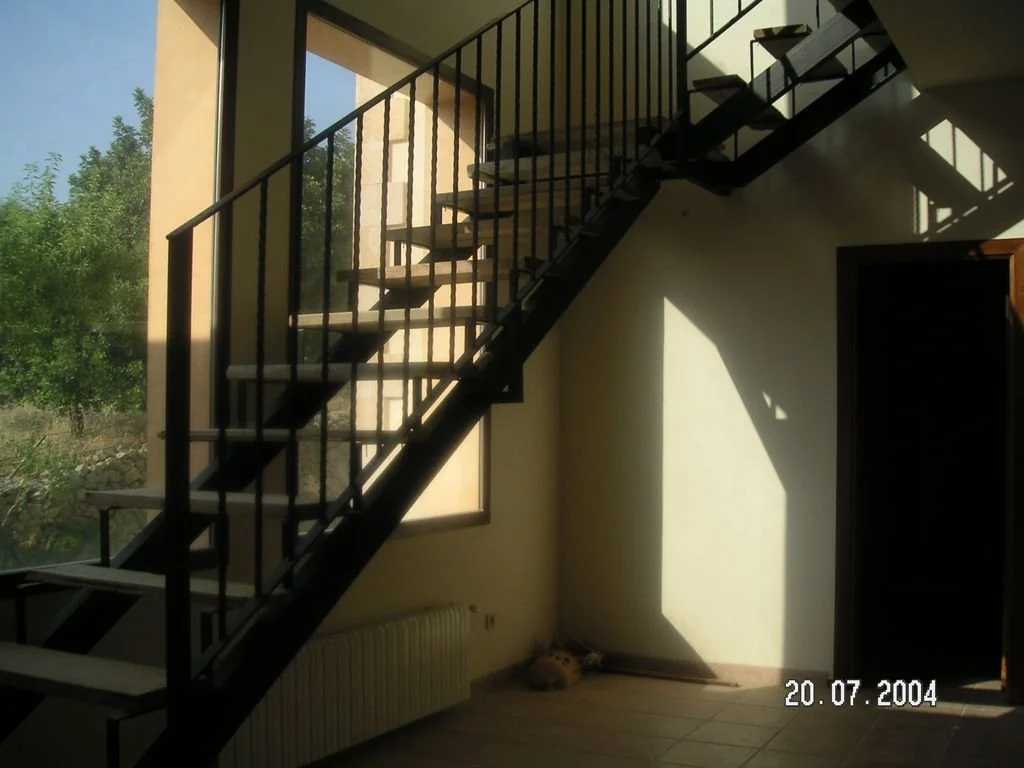 Sala con escaleras de metal negras y ventanas grandes que dejan entrar luz natural, vista exterior con árboles verdes.