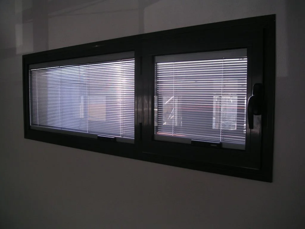 Ventana rectangular con persianas pequeñas y marco negro en la pared blanca