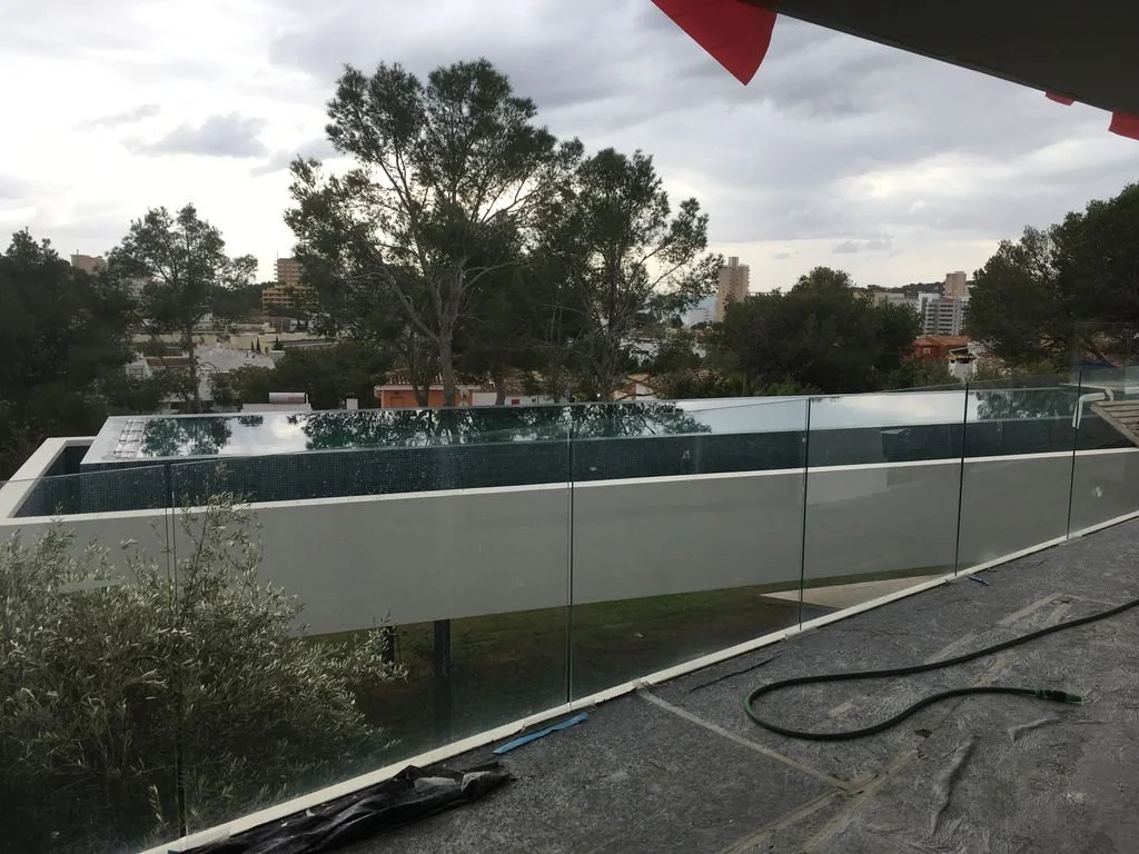 Vista desde un balcón con paredes de vidrio, árboles y edificios en el fondo, día nublado.